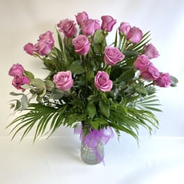 Pink roses in a glass vase with a purple ribbon