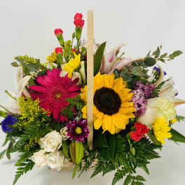Mixed bouquet with sunflowers, gerbera daisies, roses, and carnations in a wooden basket