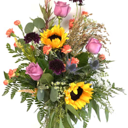 Mixed bouquet with sunflowers, pink roses, and dark purple blooms in a glass vase