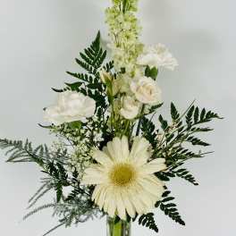 White flowers arranged in a tall glass vase with dark greenery