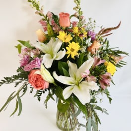 Mixed bouquet of lilies, roses, and daisies in a glass vase