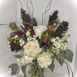 Tall arrangement of white roses and hydrangeas with dark purple calla lilies in a glass vase with curly branches.
