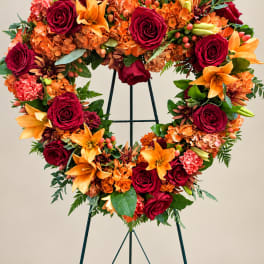Heart-shaped floral wreath with red roses, orange lilies, and orange hydrangeas on an easel