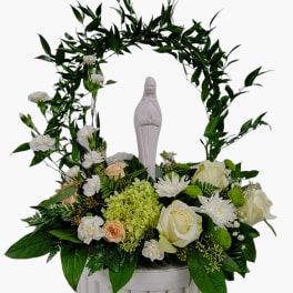 White religious statue framed by an arch of greenery and white flowers in a white container
