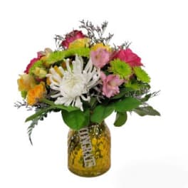 Mixed bouquet in a glass jar vase with bright pink, yellow, white, and green blooms