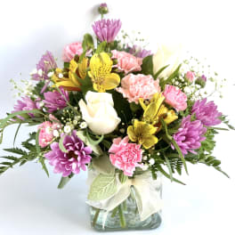 Mixed bouquet of pink, purple, yellow, and white flowers in a glass vase