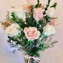 Arrangement of pink and white roses with filler flowers in a clear glass vase tied with a ribbon