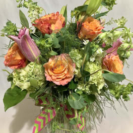 Tall arrangement of orange roses, pink lilies, and green hydrangeas in a clear glass vase
