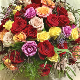Large arrangement of mixed red, yellow, peach, and lavender roses in a rounded design