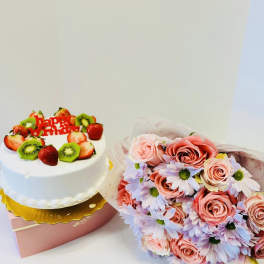 Birthday cake with fruit topping beside a pink rose and daisy bouquet
