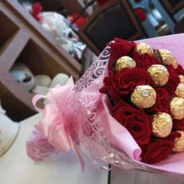 Bouquet of red roses with gold-wrapped chocolates in pink wrapping