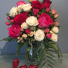 Bouquet of red, pink, and white roses in a glass vase with a red "love" decoration