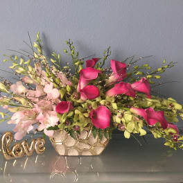 Pink and green floral arrangement in a gold vase beside a decorative "love" sign
