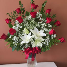 Red roses and white lilies in a clear glass vase with a red ribbon