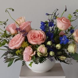 Pink roses and blue flowers arranged in a white bowl vase