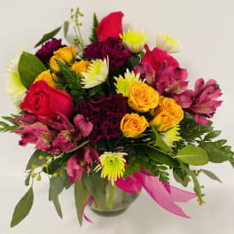 Mixed bouquet of roses and daisies in a glass vase with pink ribbon