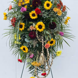Tall floral standing spray with sunflowers, roses, and carnations on an easel