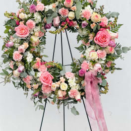 Heart-shaped floral wreath with pink and cream roses on a stand