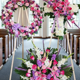 Three pink and white floral funeral tributes on easels in a church aisle