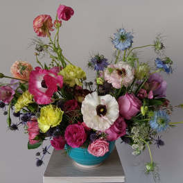Colorful mixed bouquet in a turquoise vase with pink, white, blue, and yellow blooms