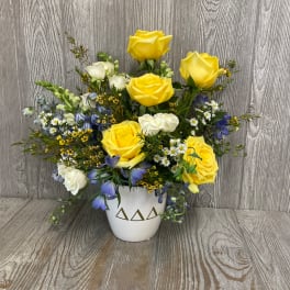 Yellow and white roses with blue flowers in a white vase