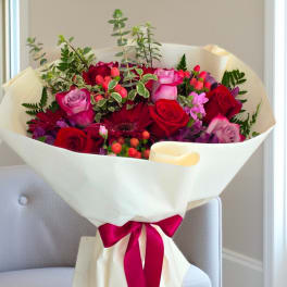 Bouquet of red and pink roses wrapped in white paper with a magenta ribbon