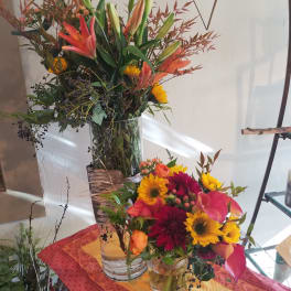 Two colorful floral arrangements in clear glass vases, one tall and one low.