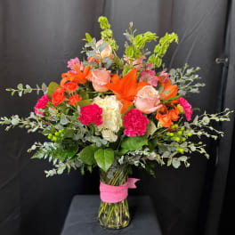 Mixed bouquet of orange lilies, pink roses, and carnations in a glass vase