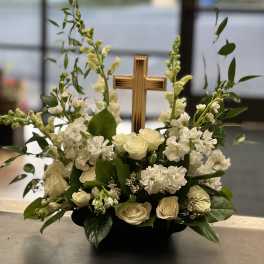 White roses and snapdragons arranged around a wooden cross