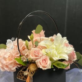 Pink and white floral arrangement in a black handbag-shaped container