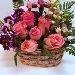 Pink roses and purple daisies in a woven basket with butterfly picks