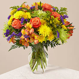 Mixed bouquet of roses, chrysanthemums, and purple filler in a glass vase