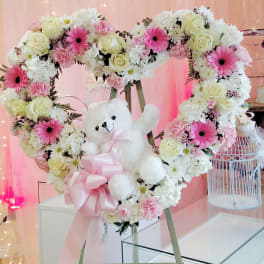 Heart-shaped floral wreath with a teddy bear and pink ribbon