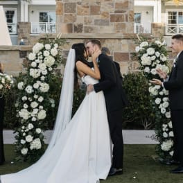 Bride and groom kissing beneath white floral wedding arches
