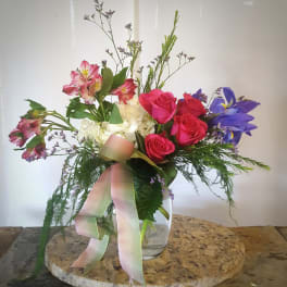 Mixed bouquet of roses, alstroemeria, and irises in a glass vase with ribbon