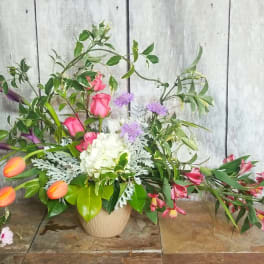 Mixed floral arrangement in a beige vase with pink, white, purple, and orange blooms