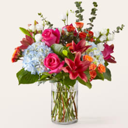 Mixed bouquet of pink roses, lilies, and blue hydrangeas in a glass vase