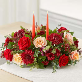 Low floral centerpiece with red and peach roses and two orange taper candles