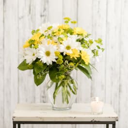 White and yellow daisy bouquet in a glass vase beside a candle