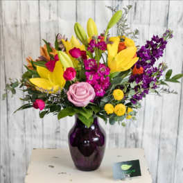 Mixed bouquet of lilies, roses, and purple flowers in a dark vase