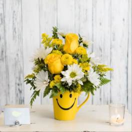 Yellow and white flower arrangement in a smiley-face mug