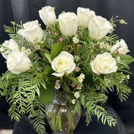 White roses arranged in a clear glass vase with mixed greenery