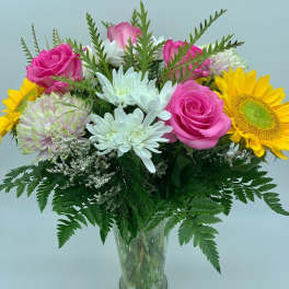 Bouquet of pink roses, white daisies, and yellow sunflowers in a glass vase