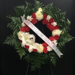 Circular funeral wreath with red and white flowers and a white ribbon