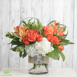 Orange roses and white hydrangeas in a glass vase with greenery