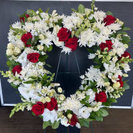 Heart-shaped floral wreath with red roses and white flowers on a stand