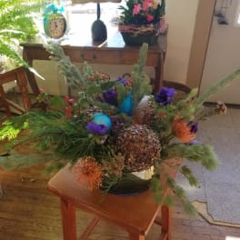 Low floral arrangement with purple and orange blooms in a dark container