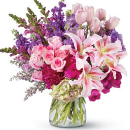 Pink lilies, roses, tulips and purple flowers arranged in a clear glass vase