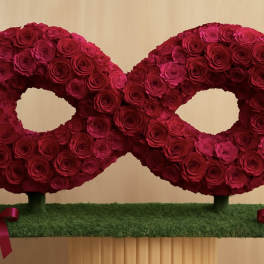 Two red rose wreaths on a grass-covered base with pink ribbons