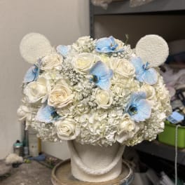 White floral arrangement with blue orchid accents on a textured stand